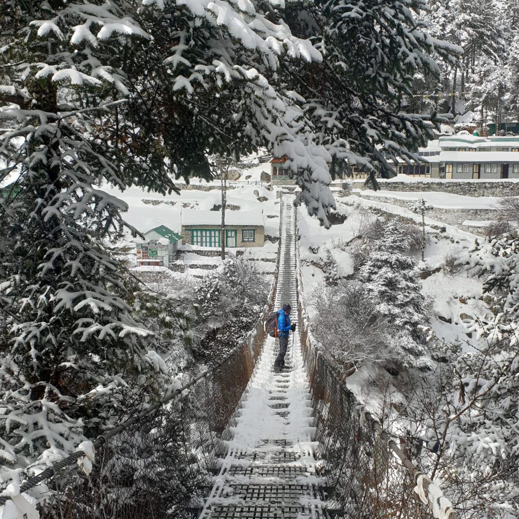 Trekker crossing a snowy suspension bridge through pine forest