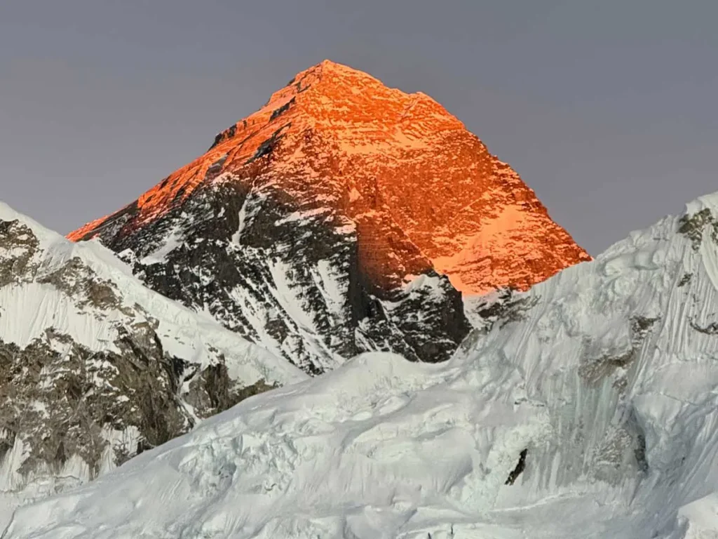 Summit of Mount Everest glowing orange at sunset above Nuptse