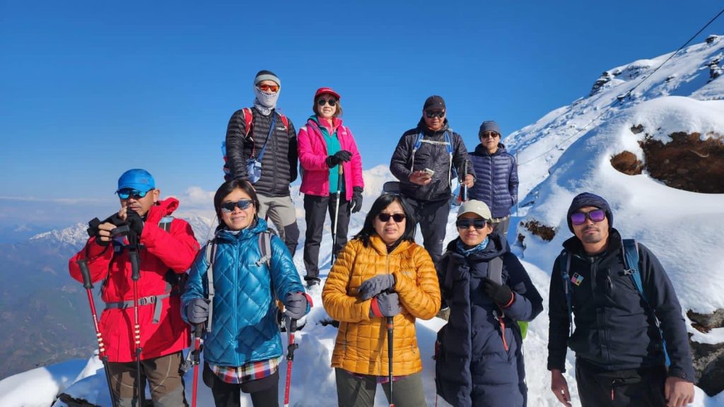 Group of trekkers in colourful down jackets posing on a snowy ridge
