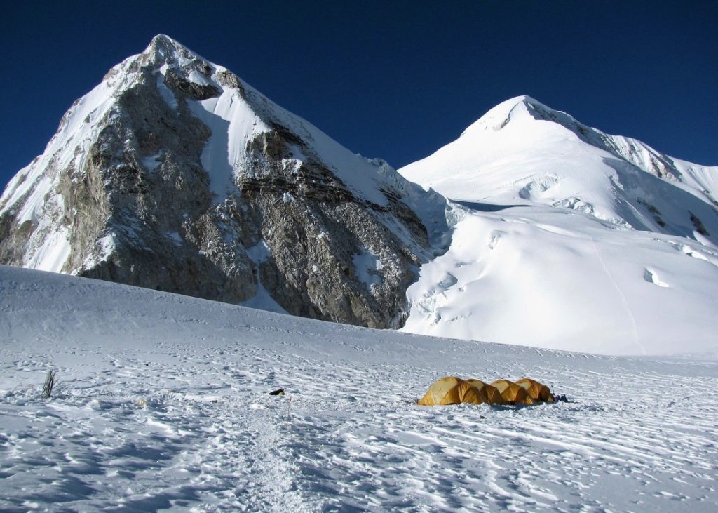 Yellow tent at a glacier camp below snowy peaks
