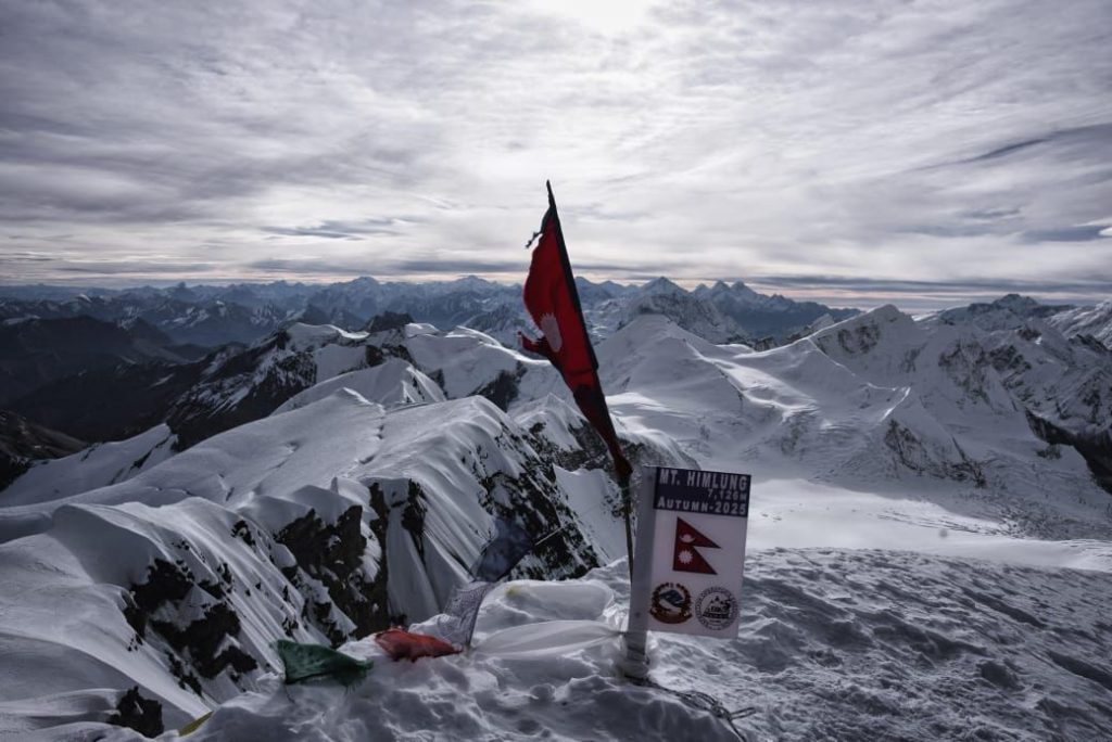 Flag of Nepal on a snowy summit with mountain ranges below