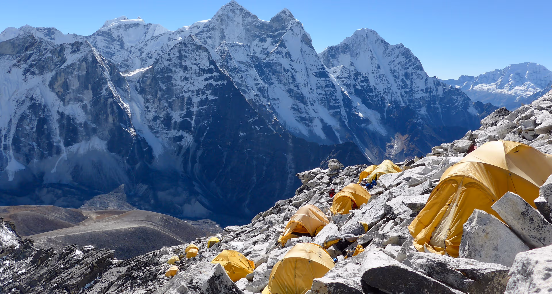 Climbers' tents on rocks below jagged snowy peaks