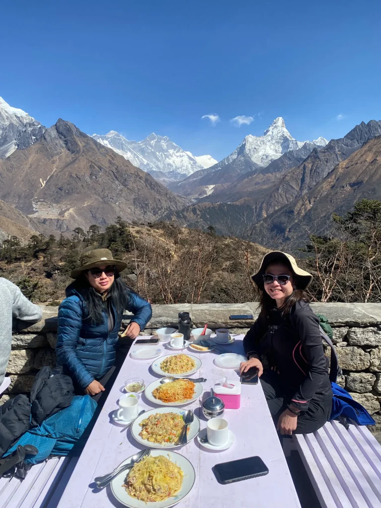 Two trekkers eating lunch at a teahouse with Everest and Ama Dablam behind