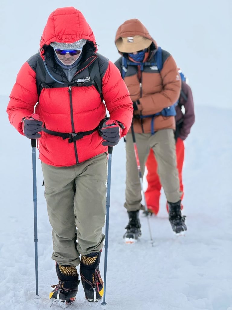 Climbers in red and orange down jackets roped together, walking up the snow of the Mera glacier with trekking poles