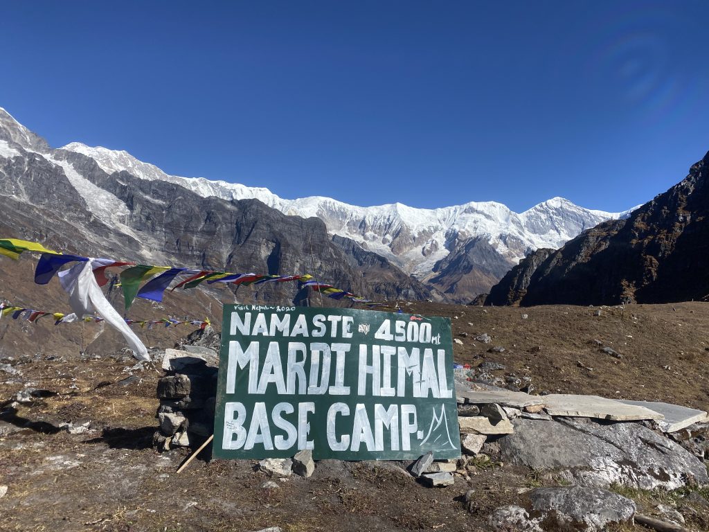 Mardi Himal Base Camp sign at 4,500 m with prayer flags and snow peaks