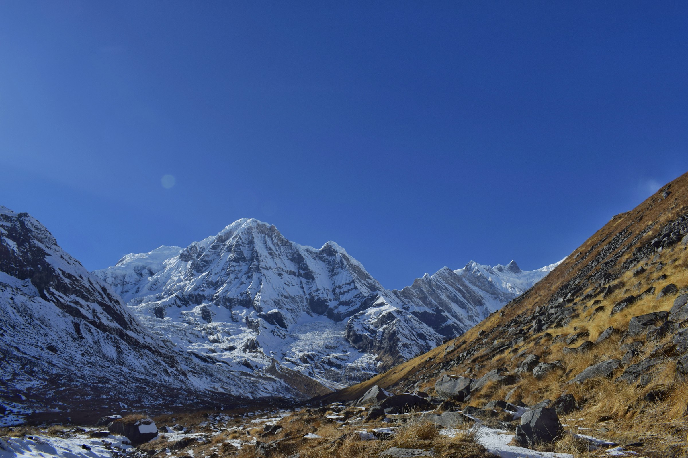 Snowy peaks at the head of a rocky glacial valley with brown grassy slopes in the Annapurna Sanctuary