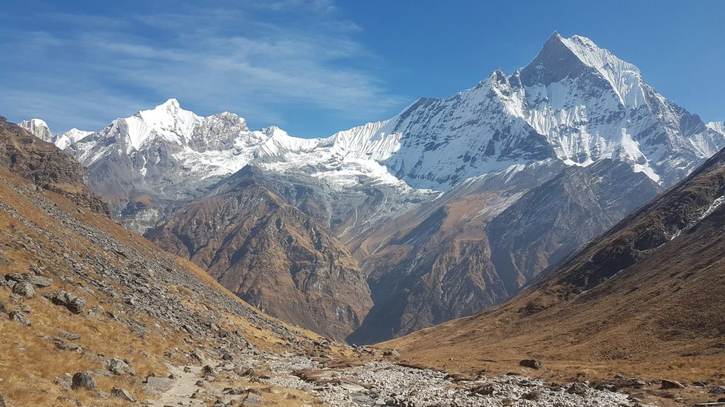Machhapuchhre's sharp summit above a rocky valley with brown grassy slopes and snowy peaks