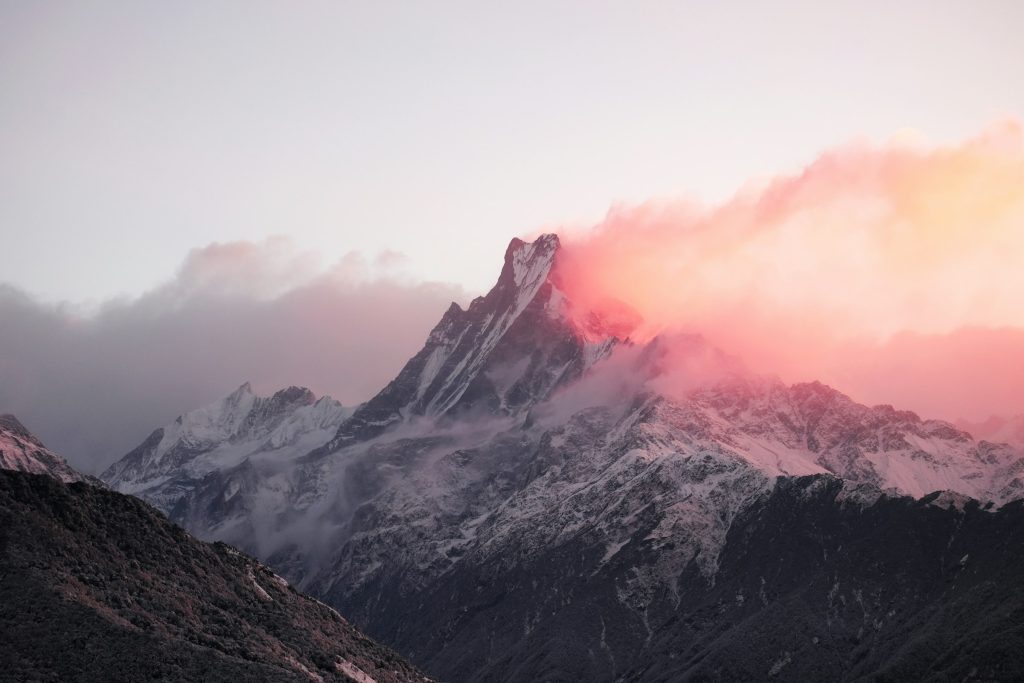 Sharp, spire-like snowy summit wrapped in pink sunset cloud above dark ridges in the Annapurna Sanctuary