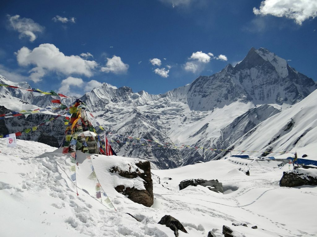 Prayer flags and snow-covered memorial cairns at a high camp with Machhapuchhre rising behind