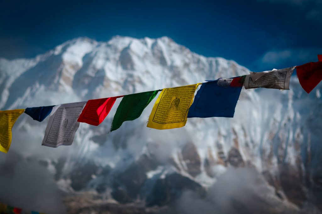Colourful prayer flags strung in front of a soft-focus snowy mountain face in the Annapurna Sanctuary