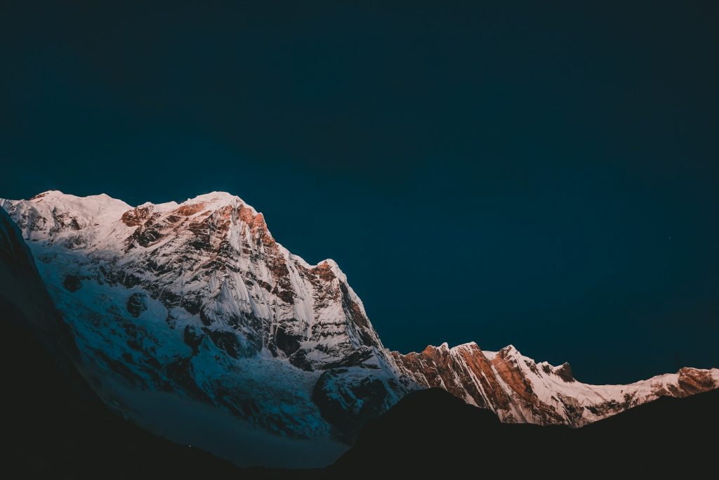 Steep snowy mountain wall catching pink first light under a dark teal sky in the Annapurna Sanctuary