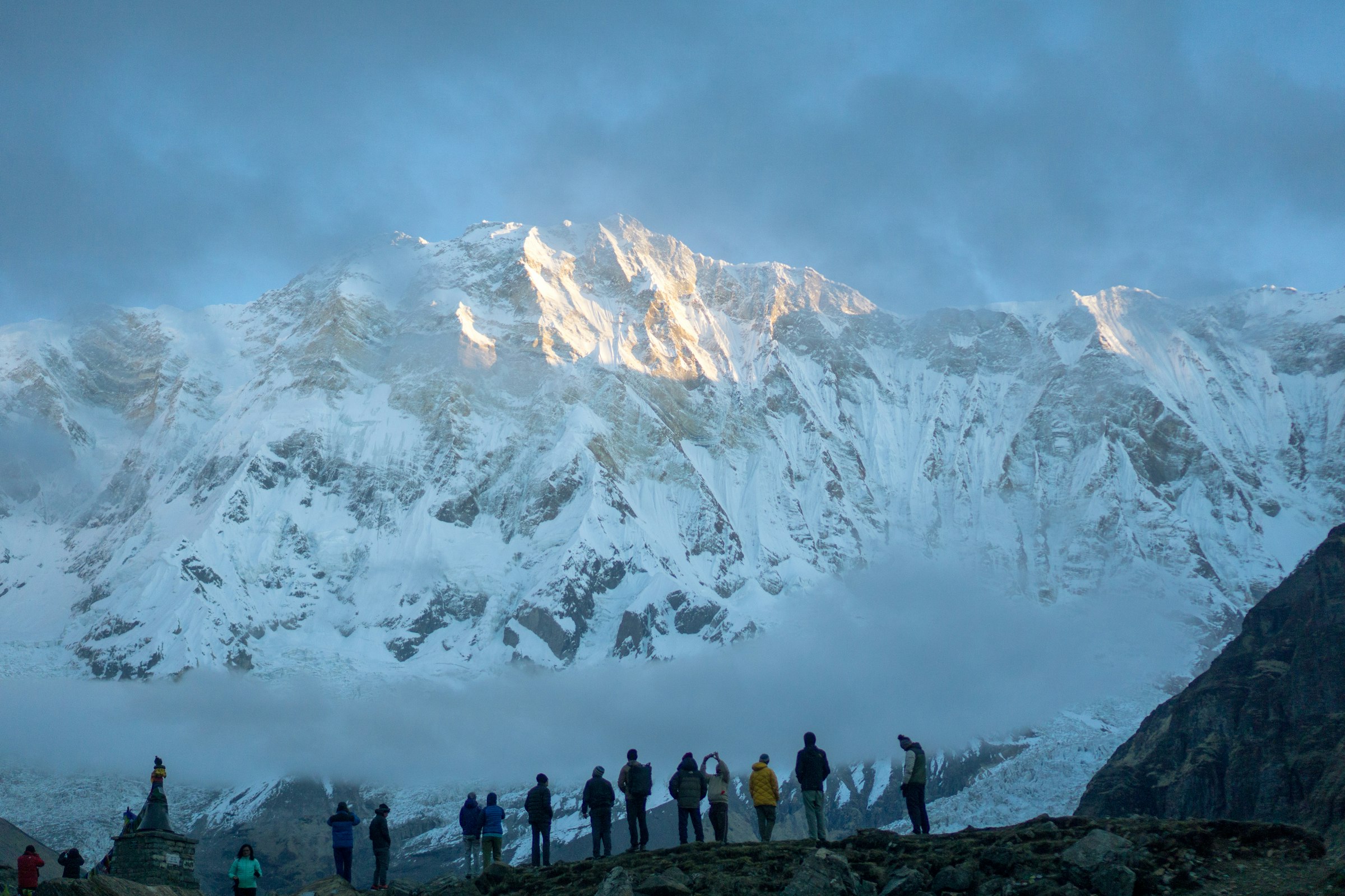 Silhouetted trekkers on a ridge watching first light strike a vast snowy wall in the Annapurna Sanctuary