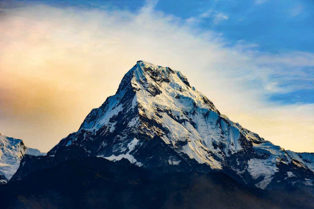 Sharp snowy pyramid peak glowing in soft light under a pastel sky in the Annapurna region