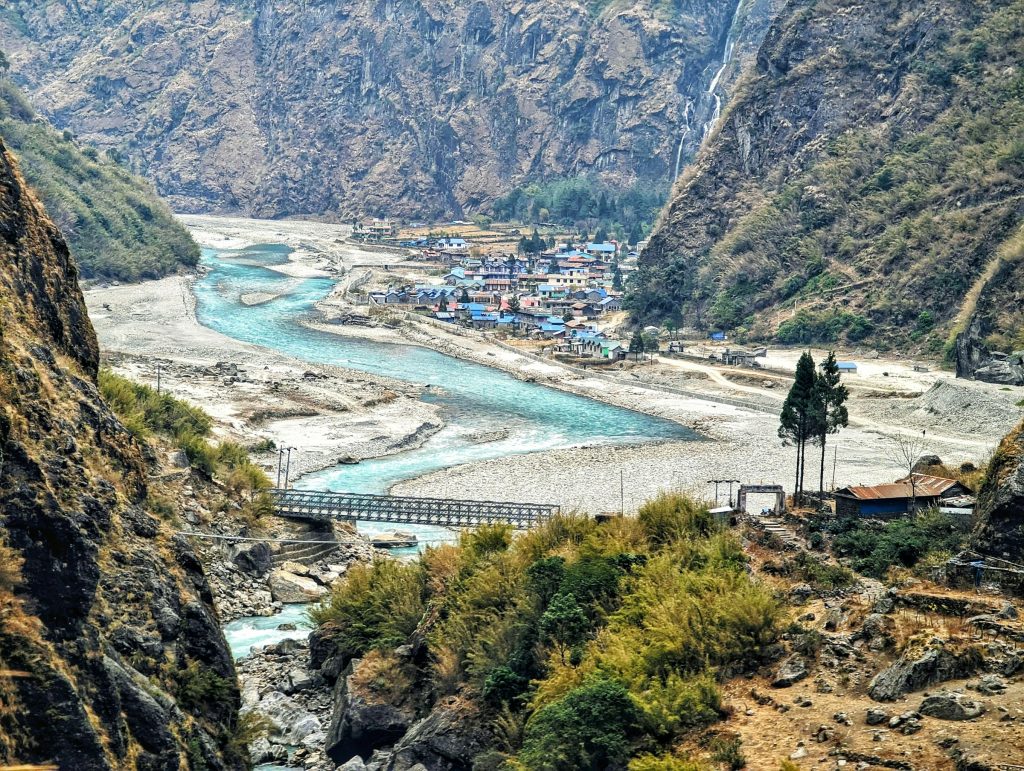 Turquoise braided river and riverside village with a suspension bridge between steep cliffs