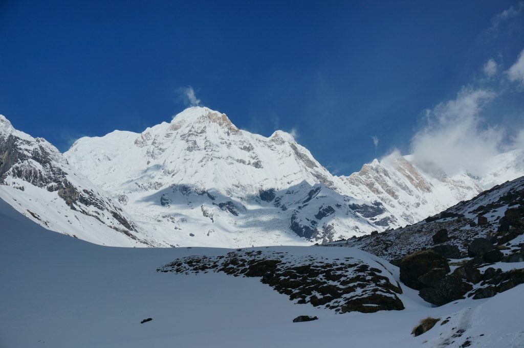 Bright snowy massif above a snowfield and dark rocks under a blue sky in the Annapurna region