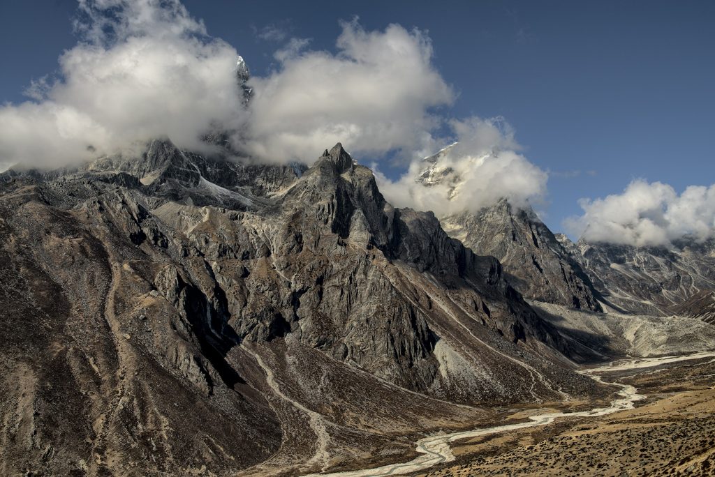 Rugged dark peaks wreathed in cloud above a winding river valley in the Everest region