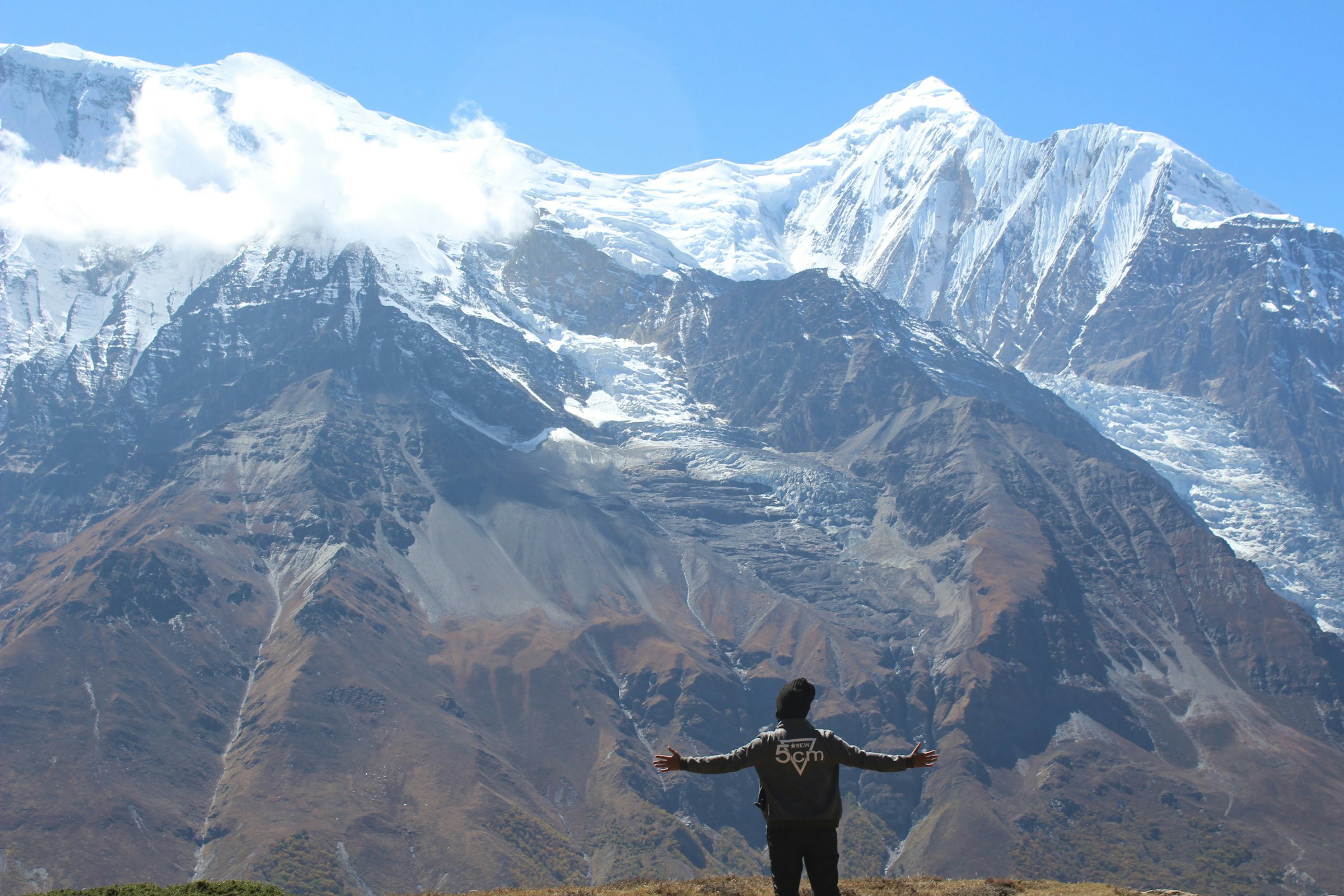 Trekker with outstretched arms facing a snowy massif with hanging glaciers in the Annapurna region