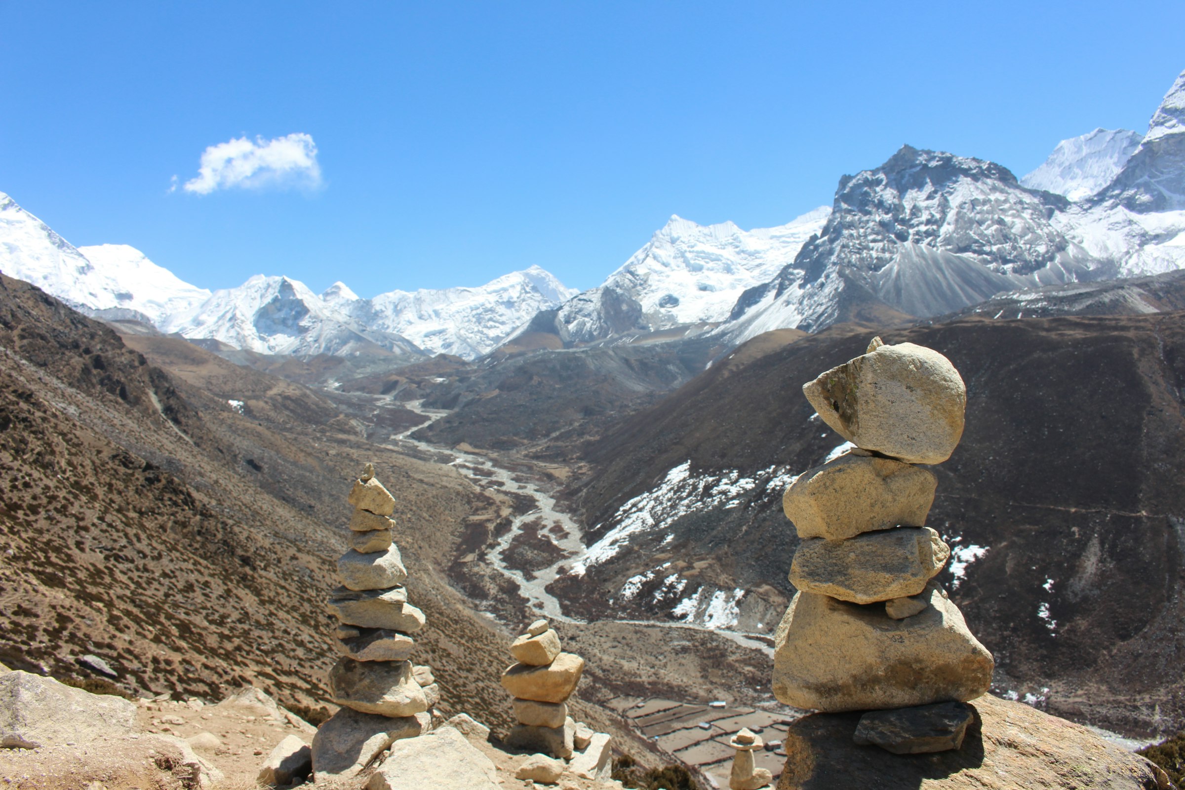 Stacked stone cairns above a winding river valley ringed by snowy peaks in the Everest region