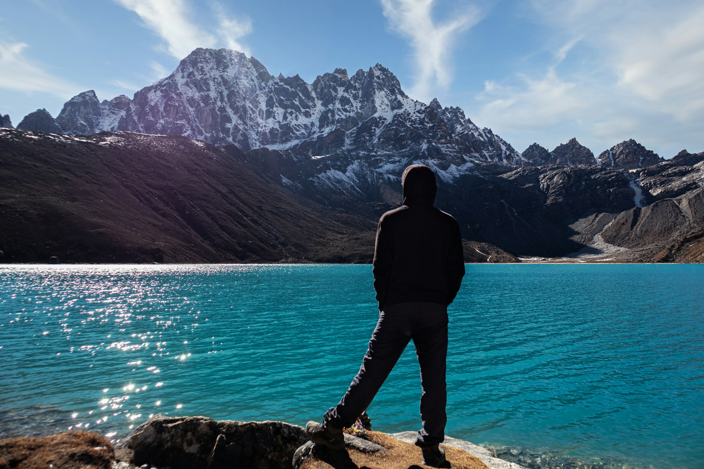 Trekker standing on a rock before a sparkling turquoise lake and jagged peaks in the Everest region