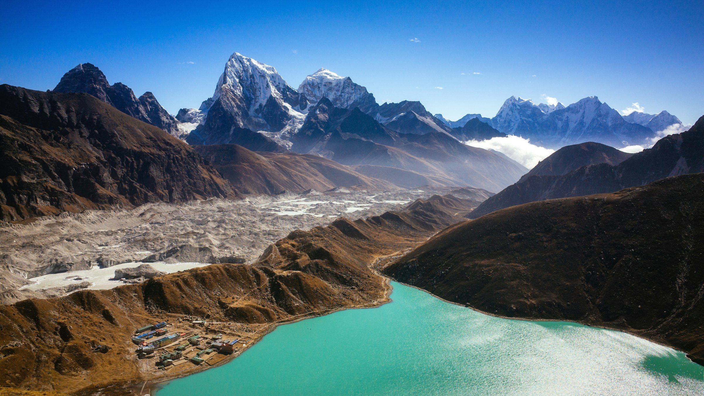 Turquoise Gokyo lake and lodges beside the rubble-covered Ngozumpa Glacier beneath jagged snowy peaks
