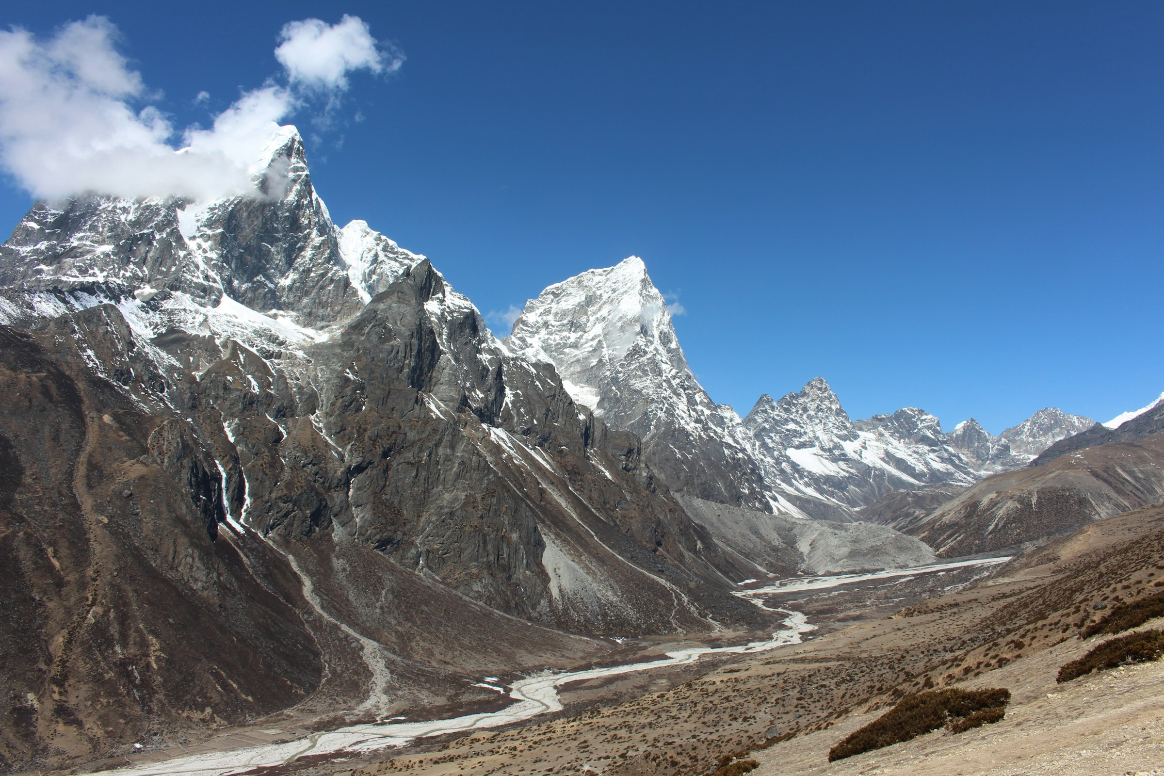 Rugged snow-streaked peaks above a wide glacial river valley under a blue sky in the Everest region