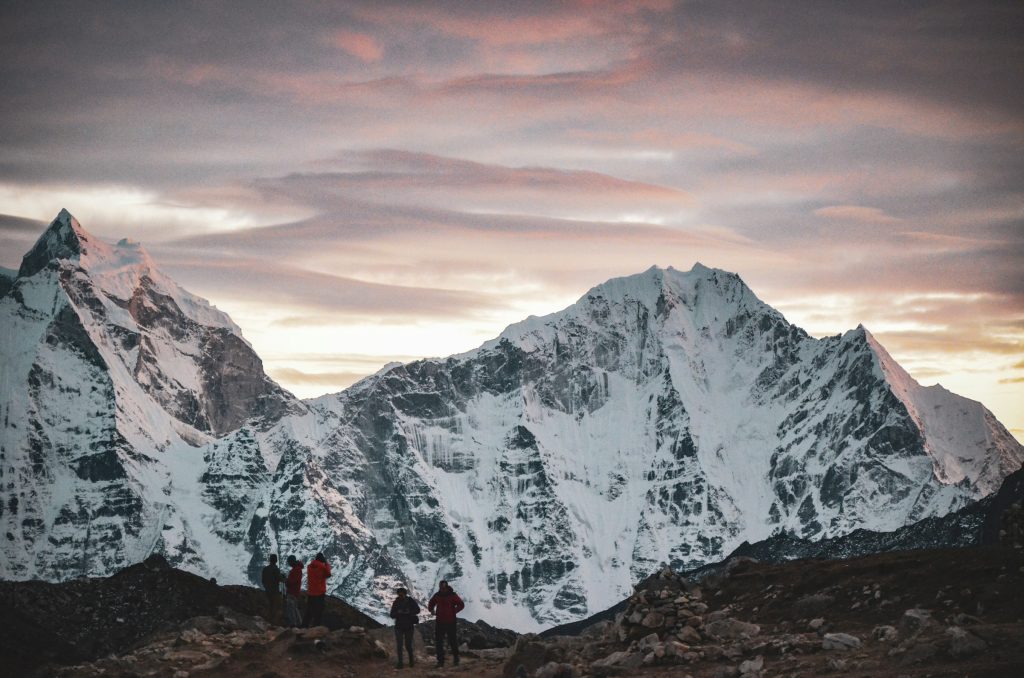 Small group of trekkers silhouetted beneath a vast snowy mountain wall at dusk in the Everest region
