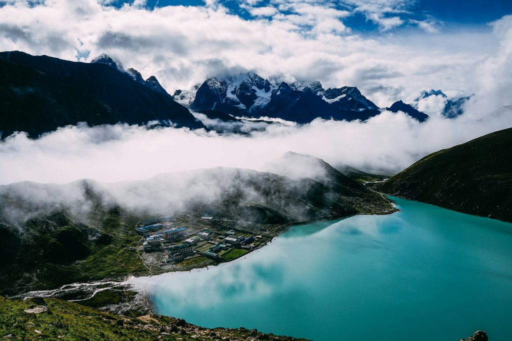 Turquoise Gokyo lake and village beneath a band of cloud and snowy peaks in the Everest region