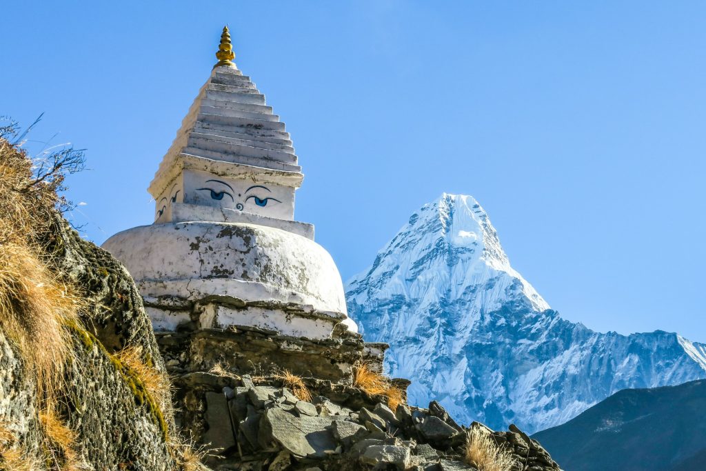 White stupa with painted Buddha eyes on a rocky slope with Ama Dablam rising behind