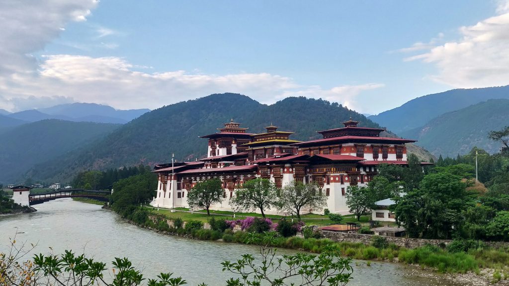 Punakha Dzong with whitewashed walls and tiered roofs beside a river below wooded hills