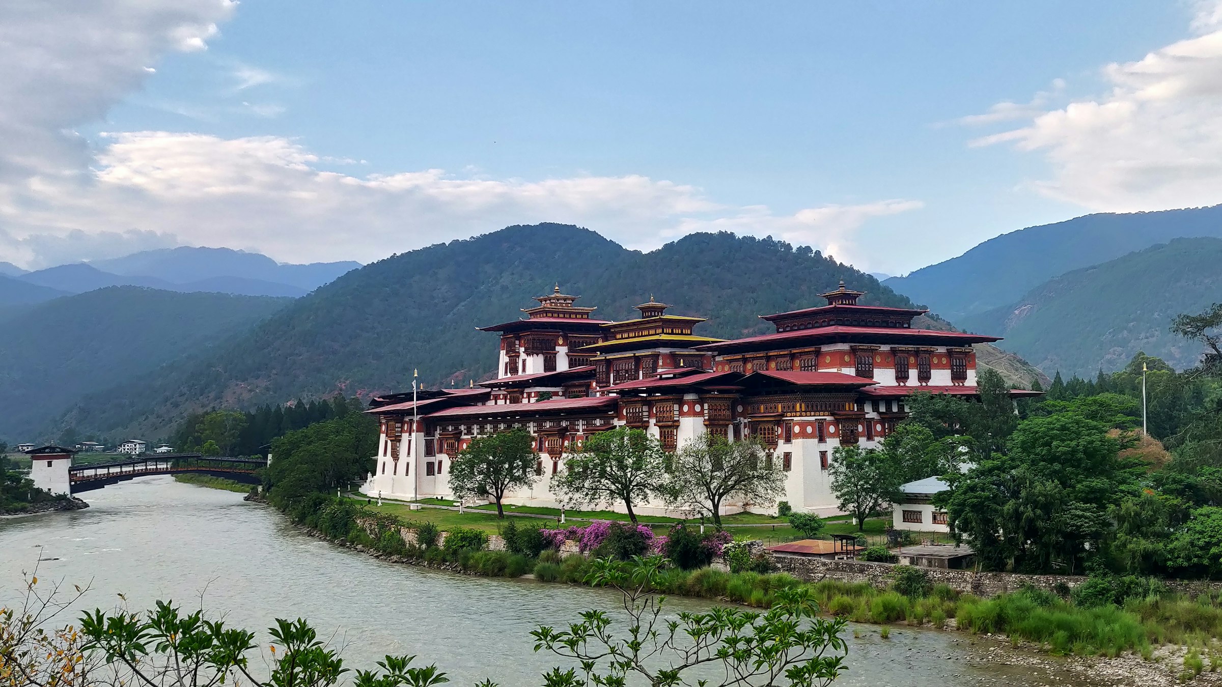 Punakha Dzong with whitewashed walls and tiered roofs beside a river below wooded hills
