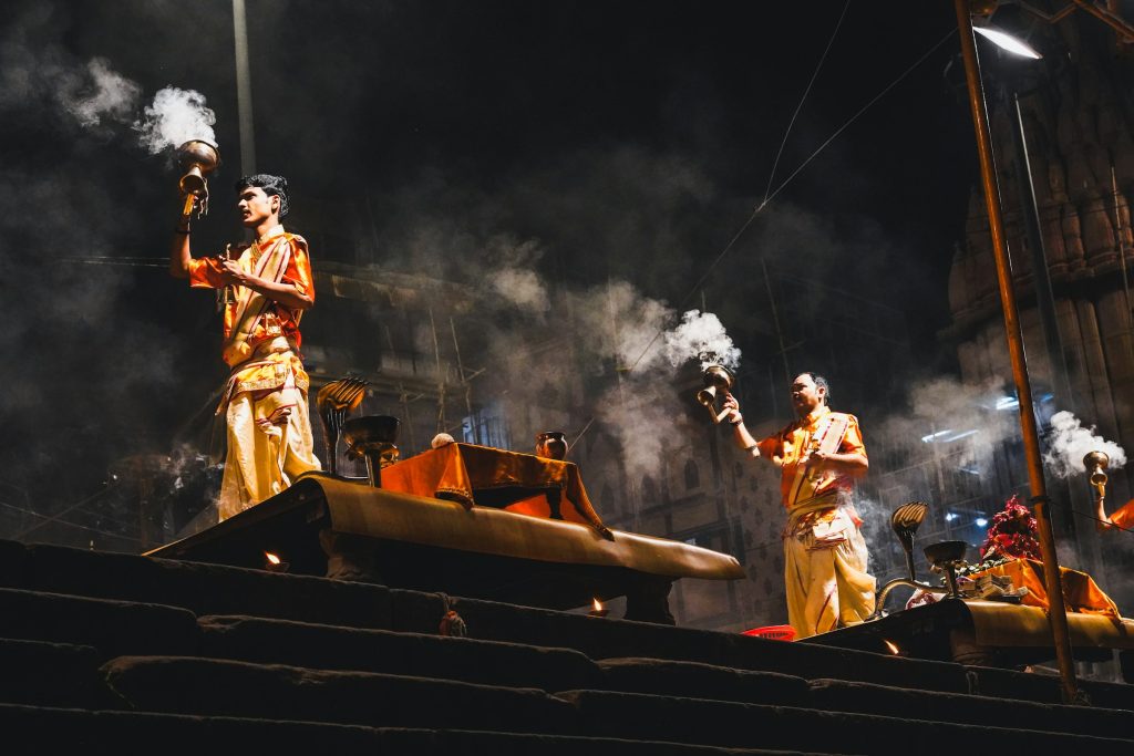 Priests in saffron robes performing the evening Ganga aarti with smoking lamps in Varanasi