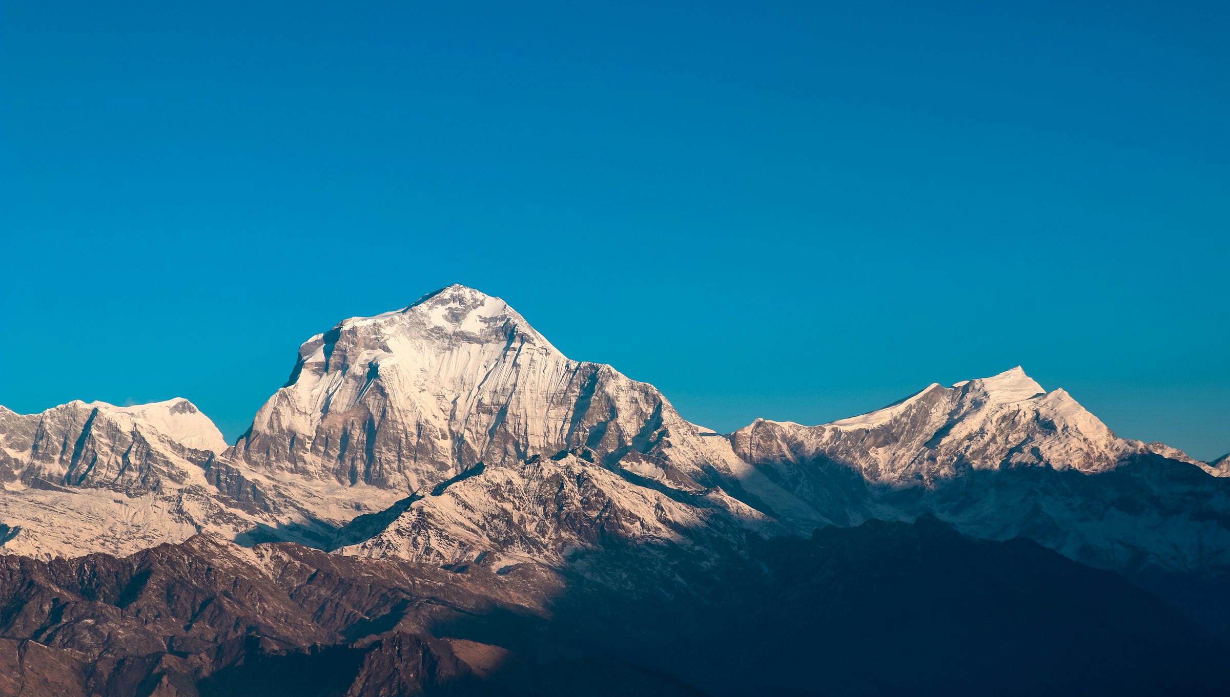 Broad snowy massif lit by morning sun above shadowed ridges under a clear blue sky