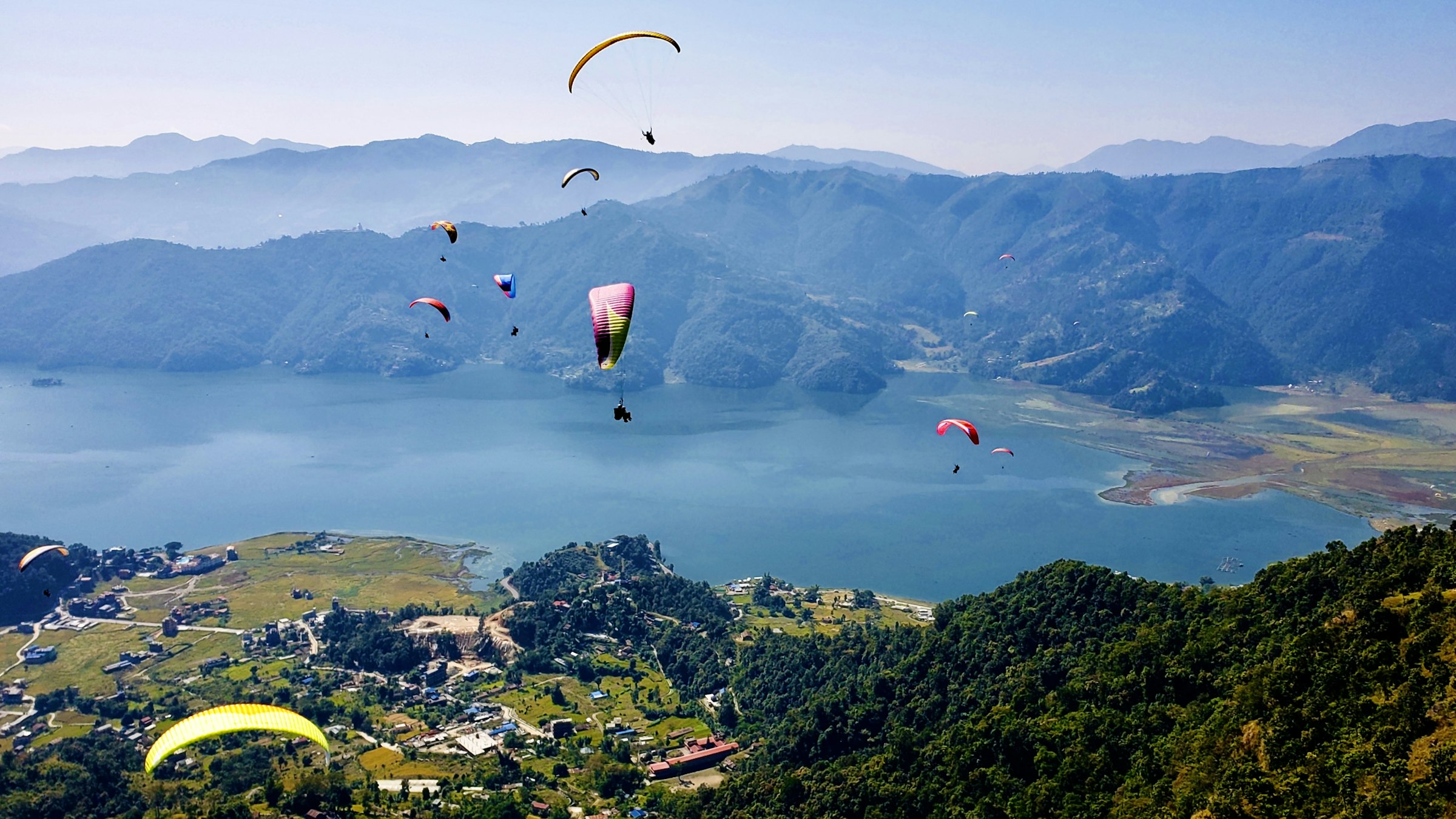 Paragliders soaring above Phewa Lake and green hills in Pokhara