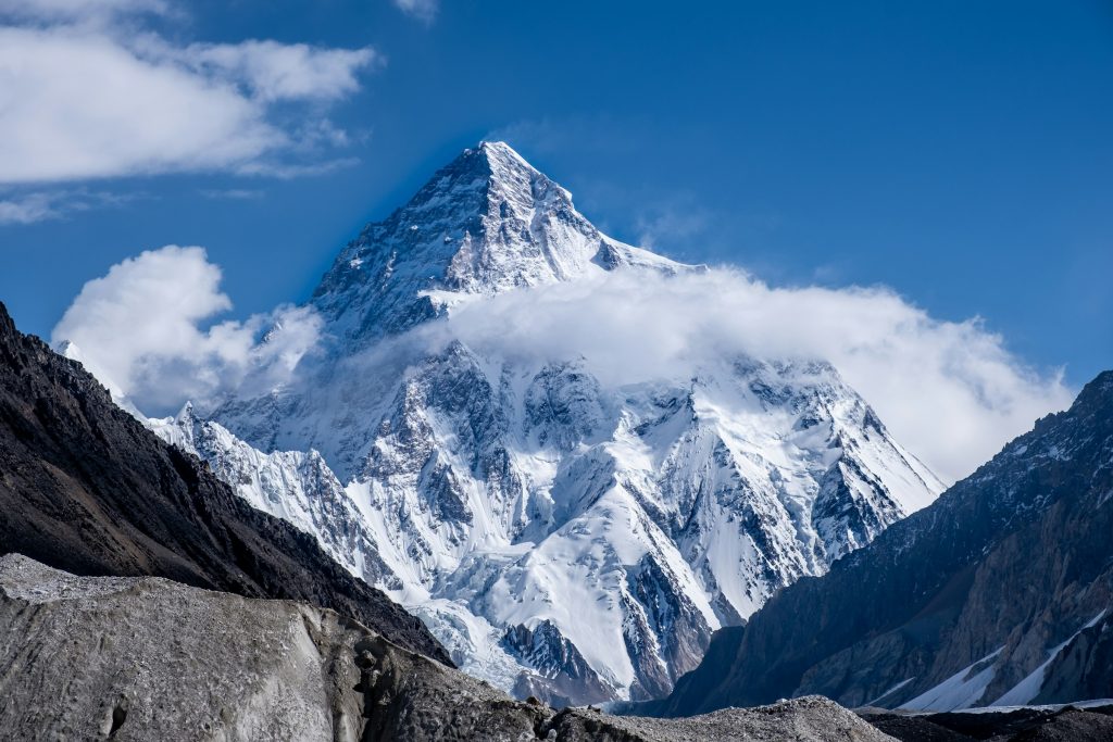 K2's pyramid summit rising above swirling cloud and rocky glacier moraine in the Karakoram