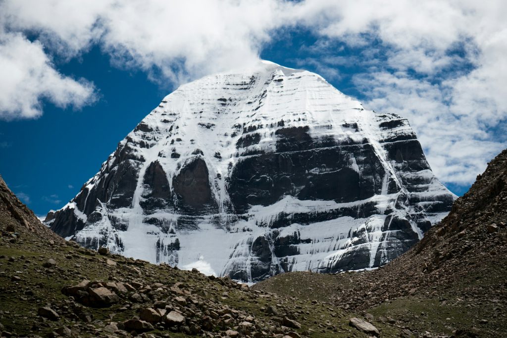 Snow-streaked north face of Mount Kailash rising above a rocky valley under cloud