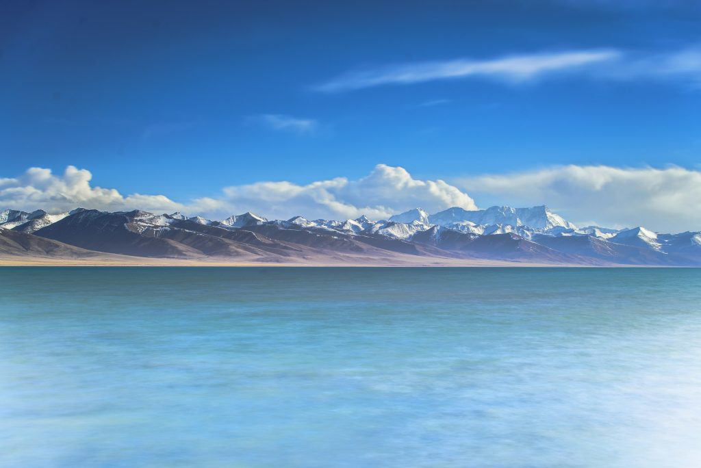 Calm blue lake stretching towards a distant snowy range under a wide sky in western Tibet