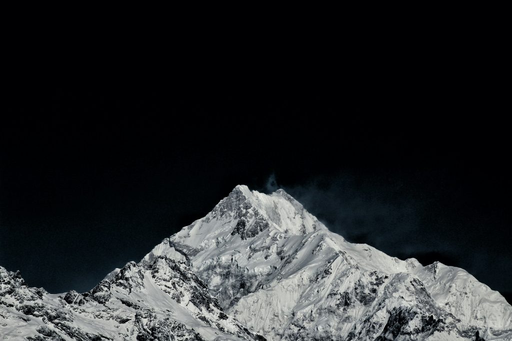 Pointed snowy summit with a wisp of blown snow against a black sky in the Kangchenjunga region
