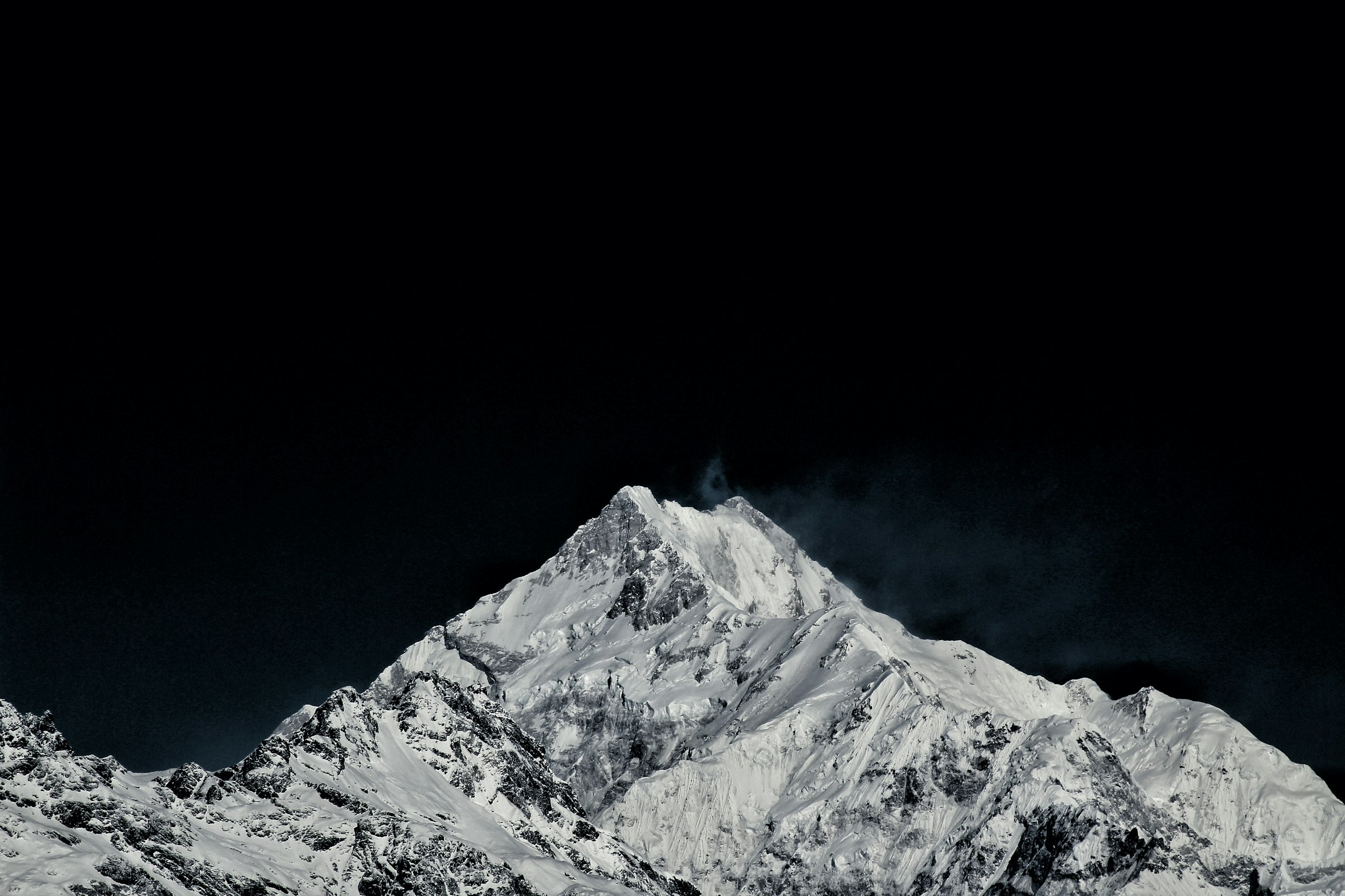 Pointed snowy summit with a wisp of blown snow against a black sky in the Kangchenjunga region