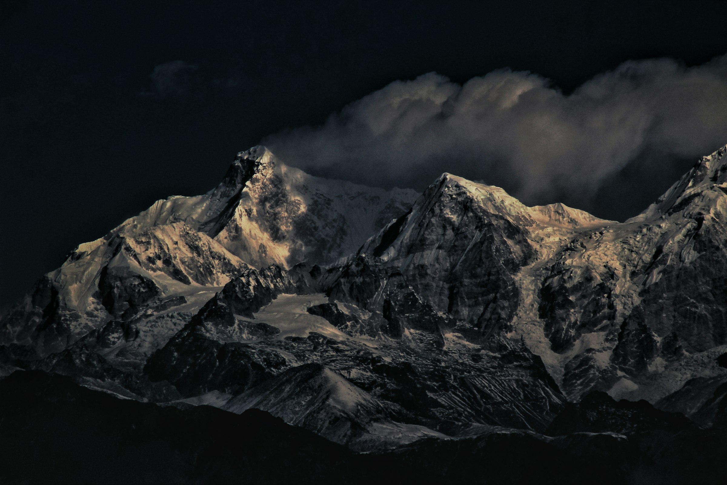 Rugged snowy ridges in dramatic dark light with cloud streaming off the summits in the Kangchenjunga region