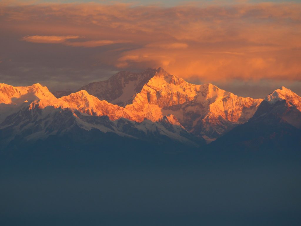 Snowy massif glowing orange at sunrise above layers of blue haze in the Kangchenjunga region