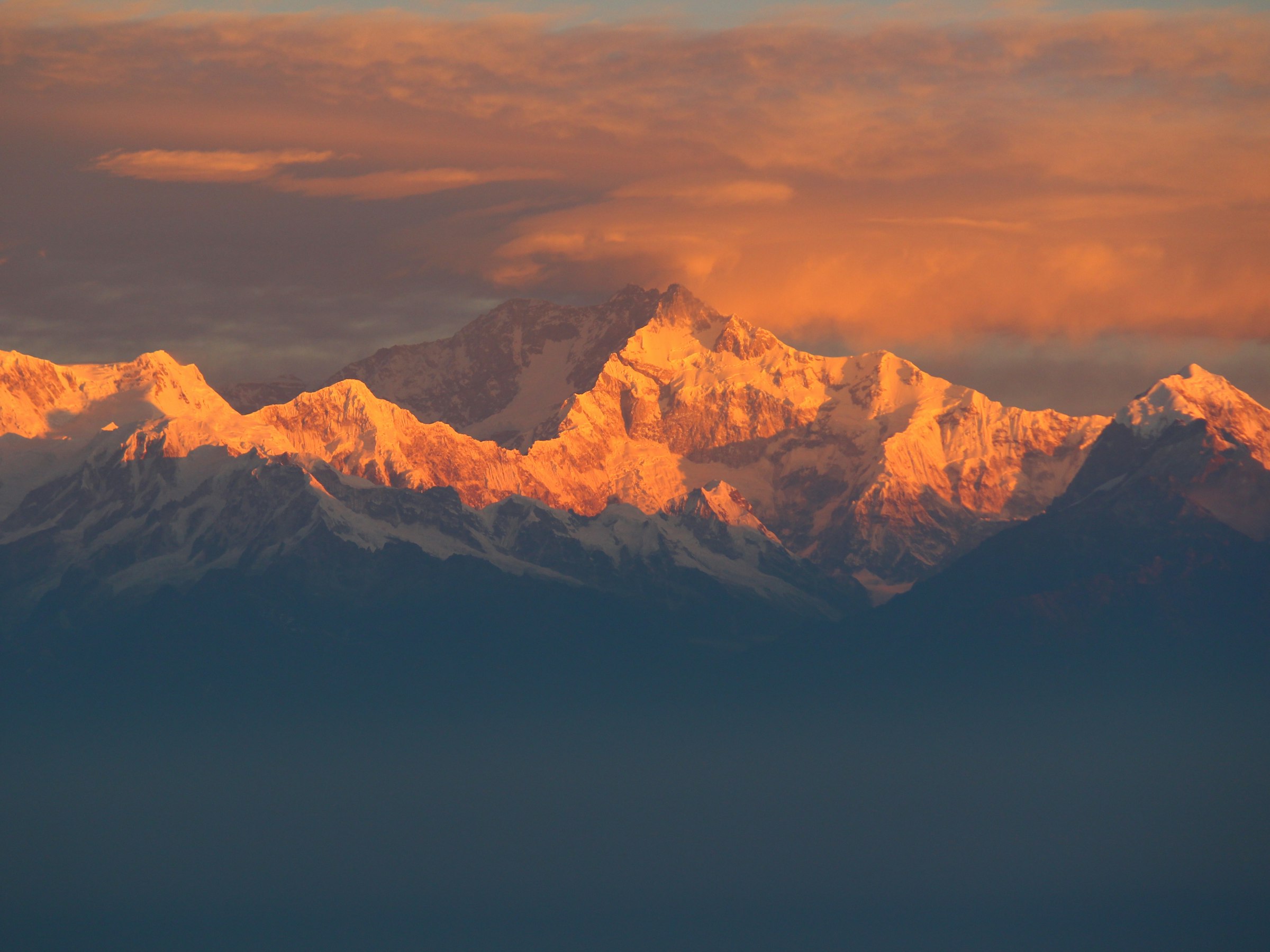 Snowy massif glowing orange at sunrise above layers of blue haze in the Kangchenjunga region