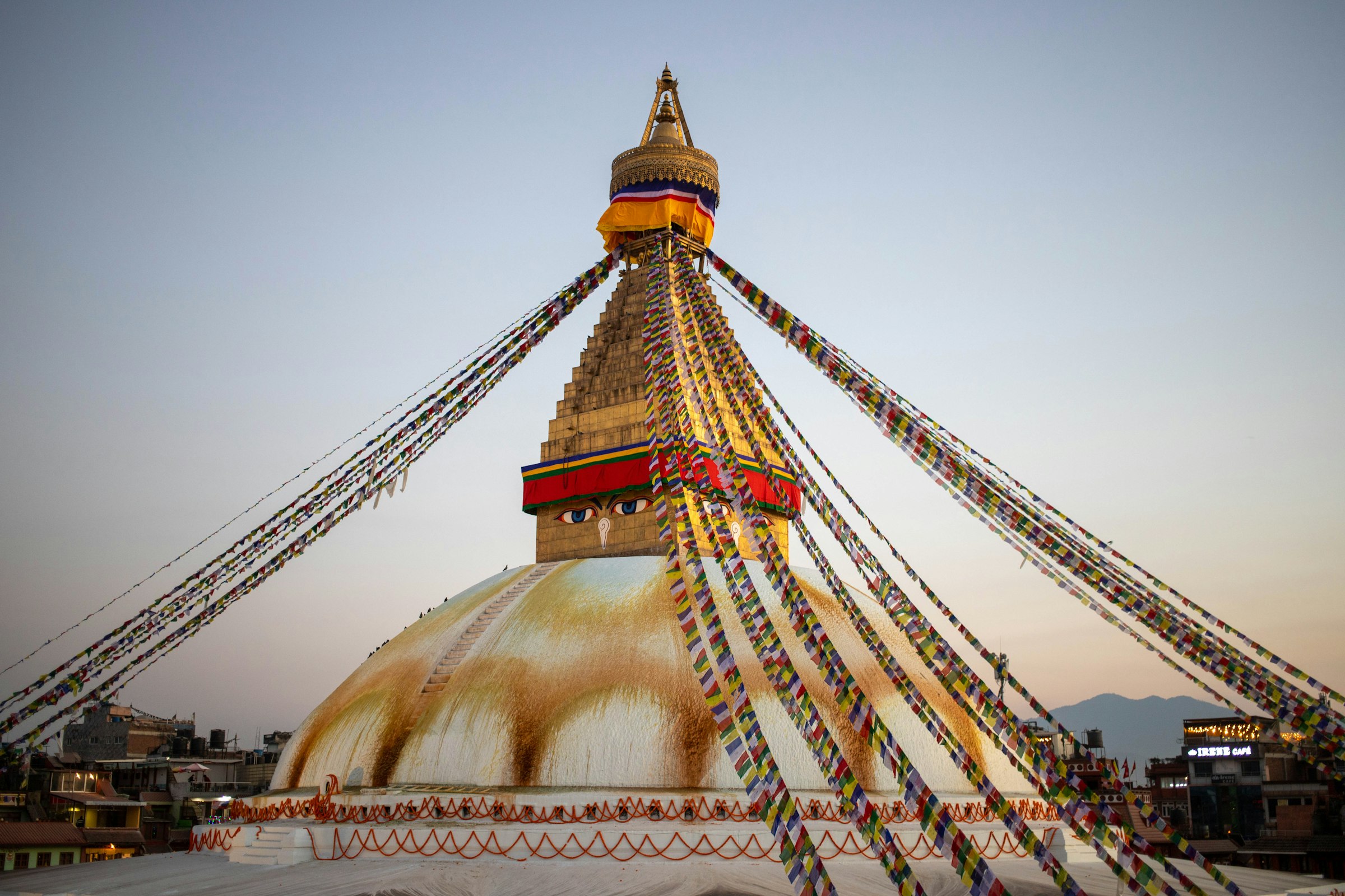 Boudhanath stupa's golden spire and white dome with radiating strings of prayer flags at dusk