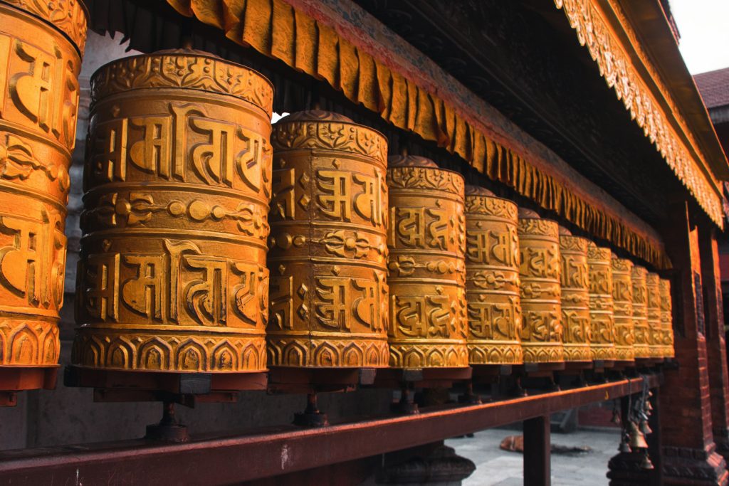 Row of golden prayer wheels embossed with Buddhist mantras beneath a carved wooden eave