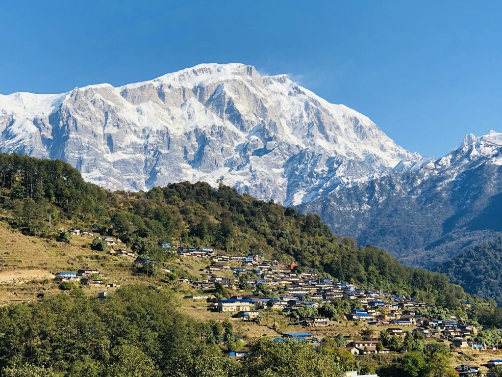 Hillside village of blue-roofed houses below a vast snowy mountain wall in the Annapurna region
