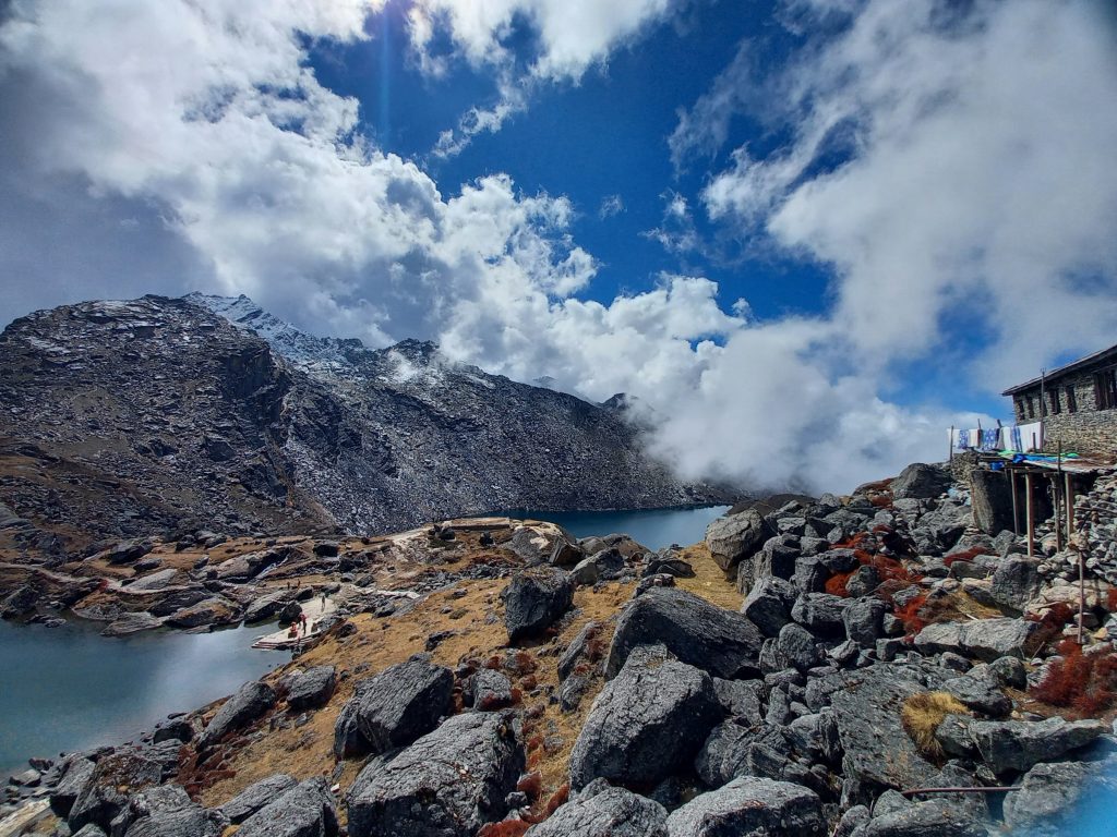 Alpine lake below rocky slopes and dramatic clouds with a boulder-strewn shore in the Langtang region