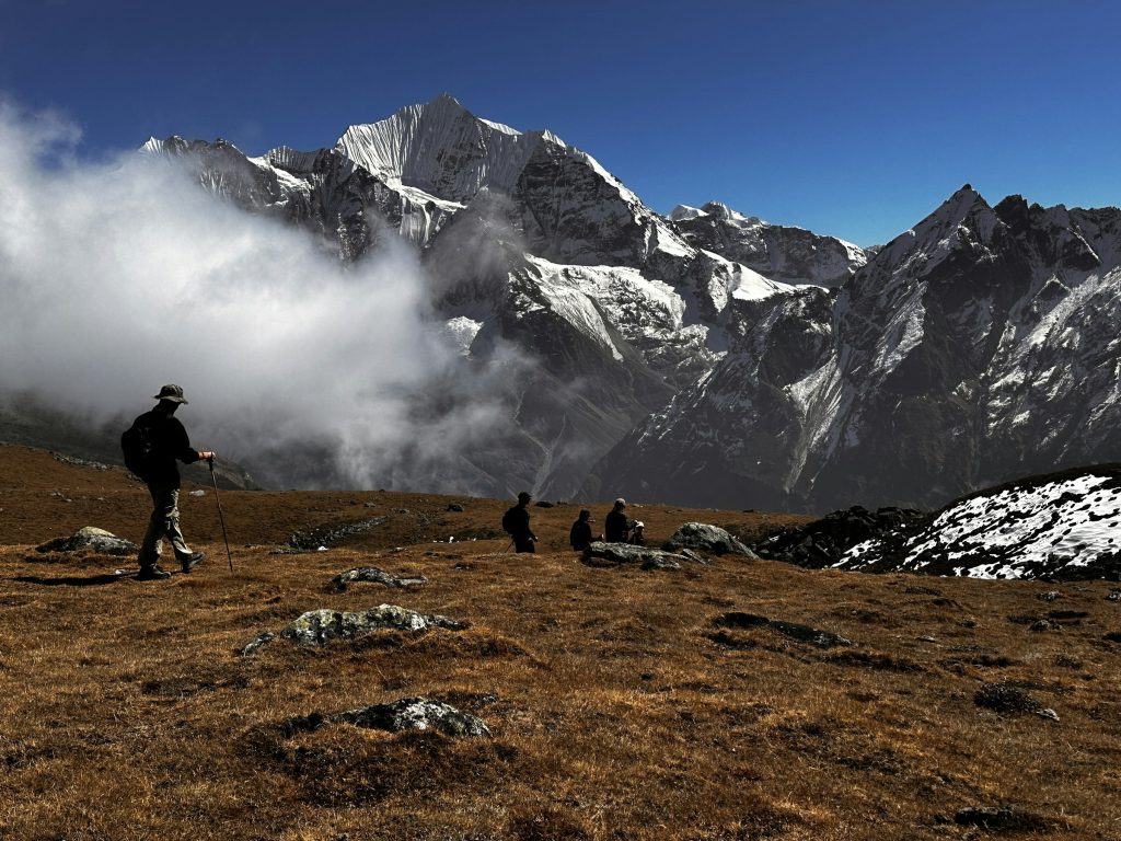 Trekkers crossing a brown alpine meadow below a snow-capped peak and drifting cloud in the Langtang region