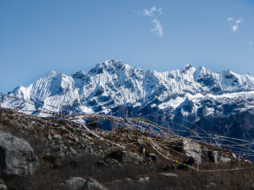 Jagged snow-covered range behind a rocky hillside strung with prayer flags in the Langtang region