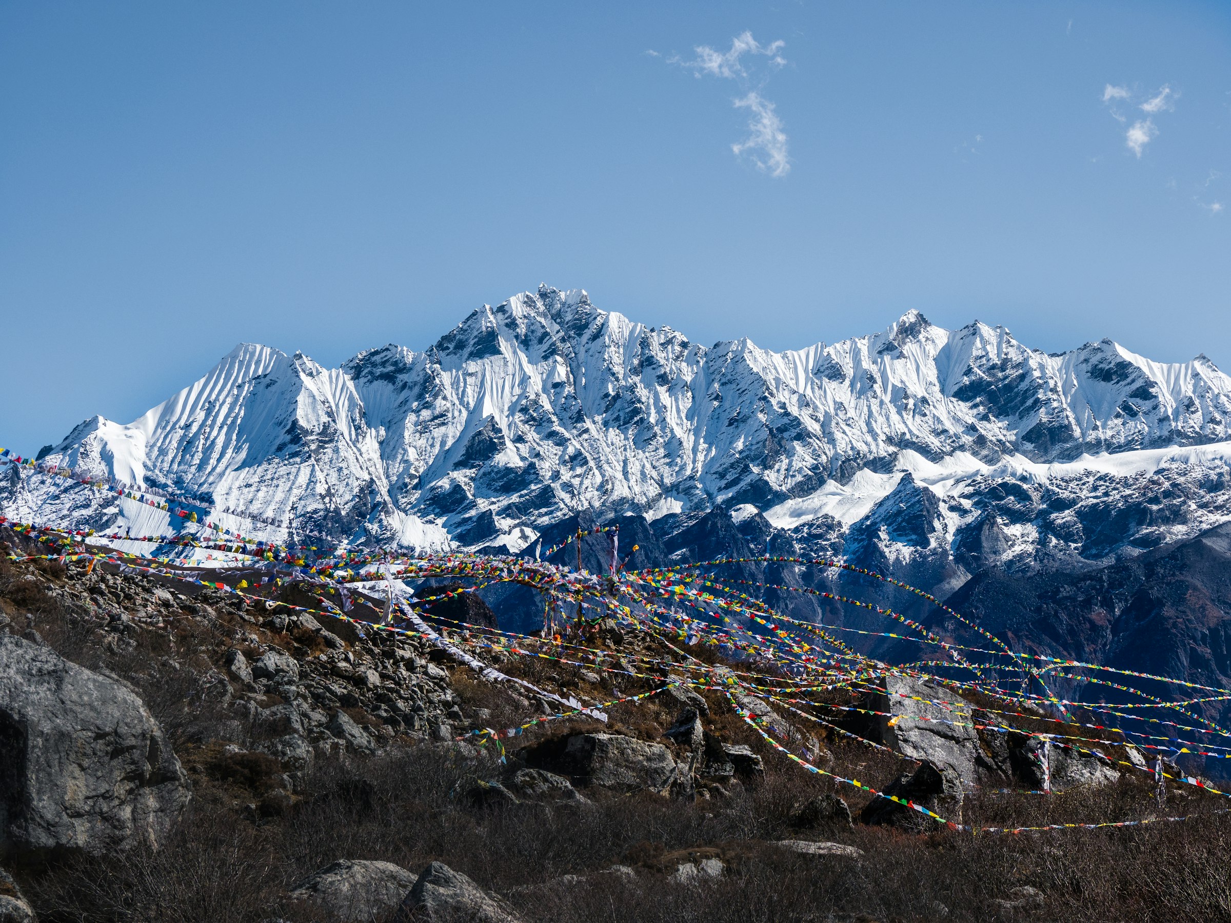 Jagged snow-covered range behind a rocky hillside strung with prayer flags in the Langtang region
