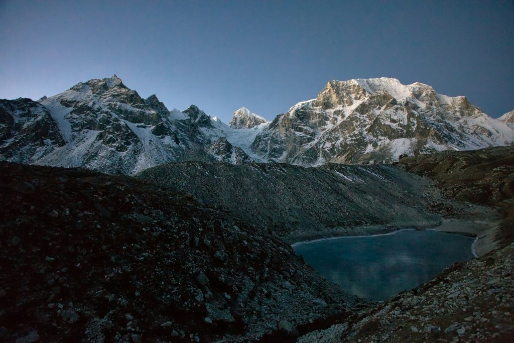 Dark glacial lake cradled by moraine below rugged snowy peaks in the Manaslu region