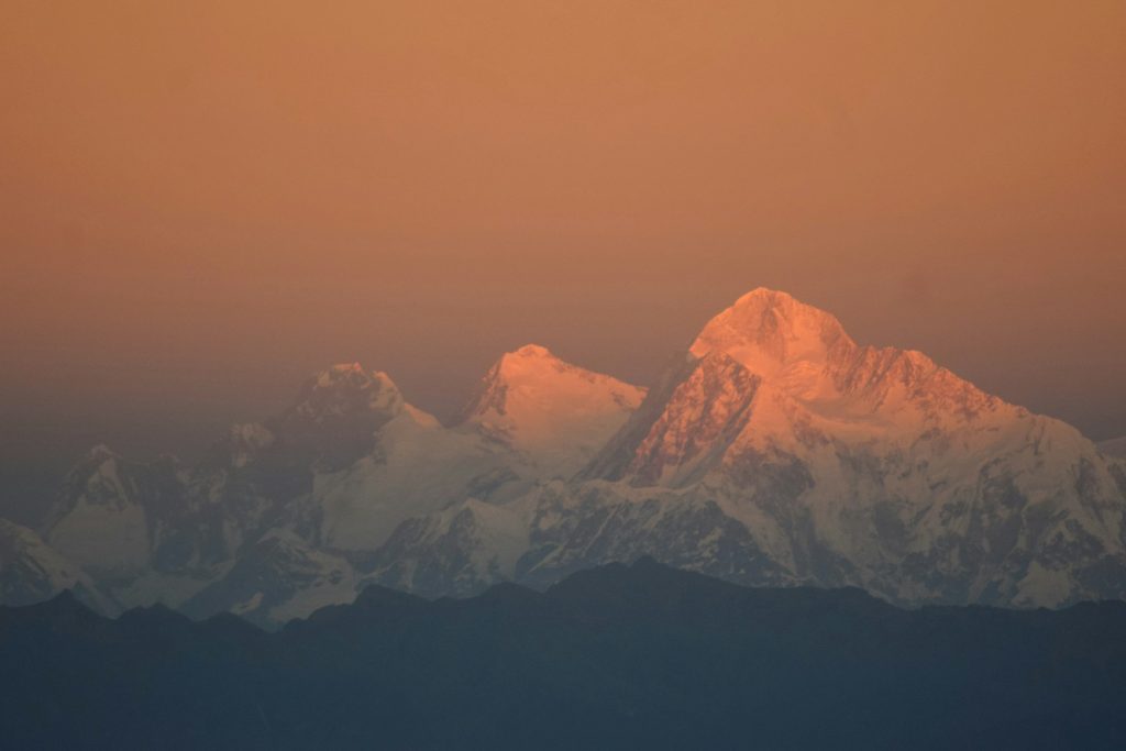 Snowy summits glowing orange at sunset above hazy blue ridges in the Makalu region